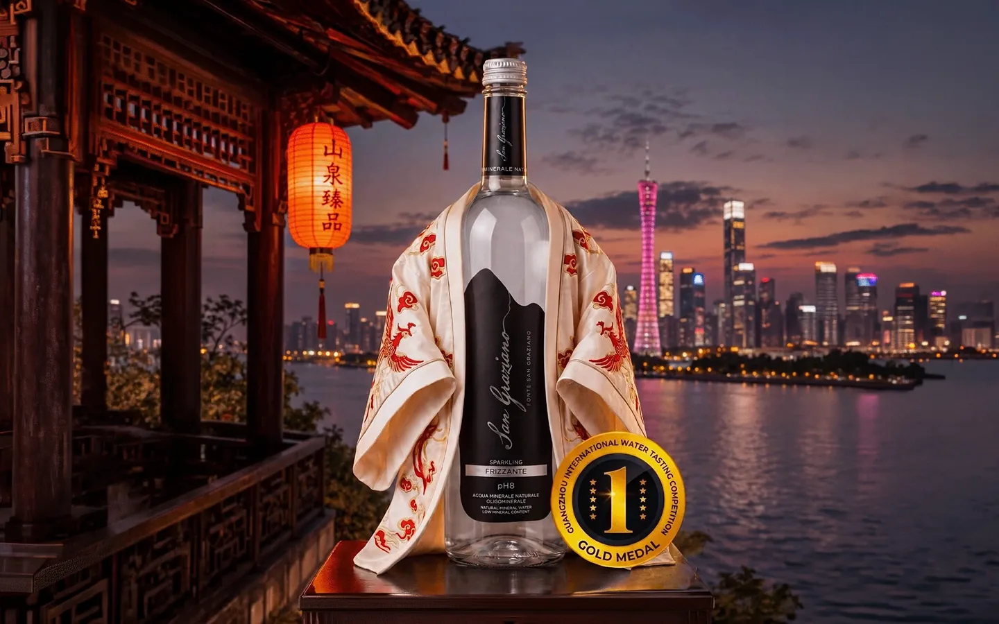 Bottiglia San Graziano Frizzante con veste cinese ricamata davanti allo skyline di Canton al tramonto, con il sigillo Gold Medal della Guangzhou International Water Tasting Competition